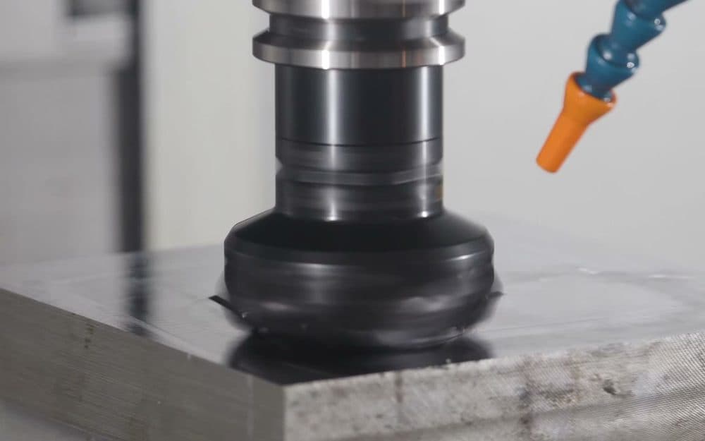 An abrasive head on a vertical spindle running across the face of a steel plate.